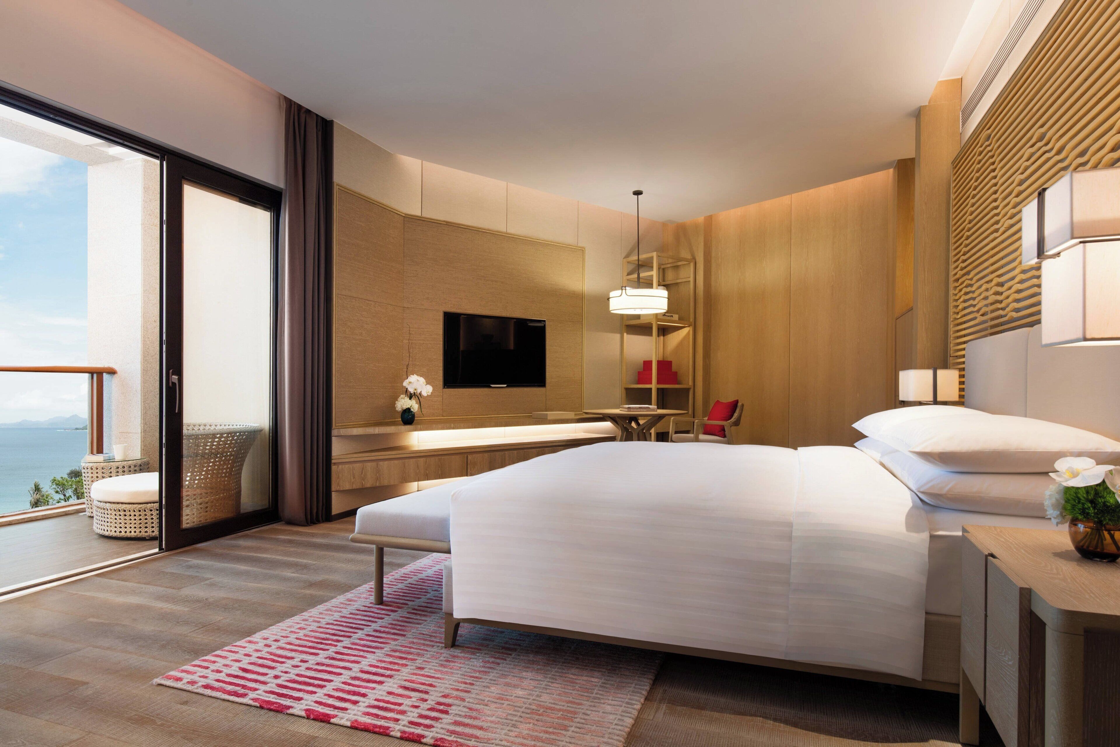 A modern hotel room with a large bed, a TV, a bathroom, and a balcony with a view.