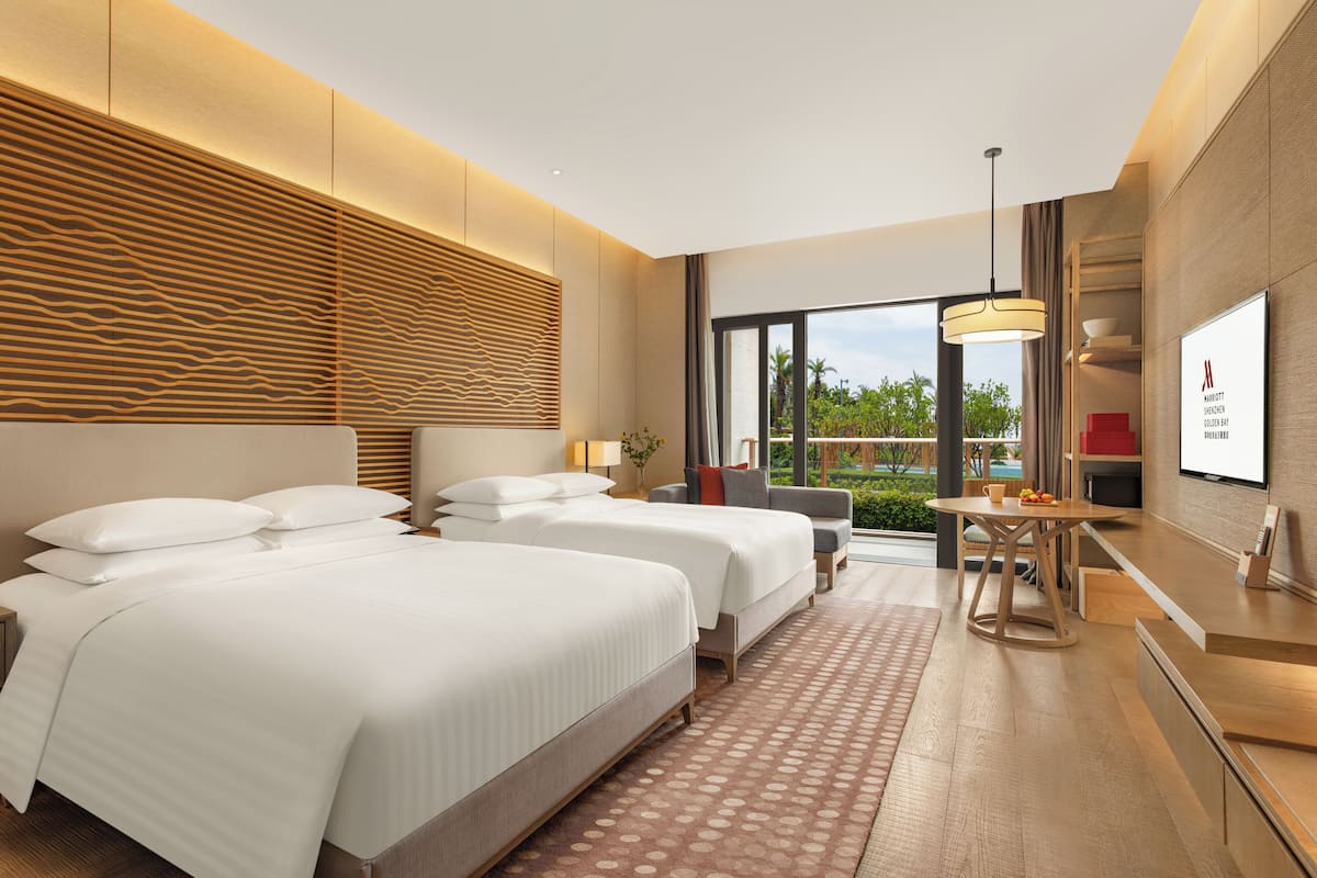 Ett modernt hotellrum med två sängar, en matplats och ett stort fönster med utsikt över grönområden.