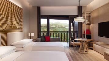 A hotel room with a large bed, a desk, a chair, a TV, and a balcony with a view of the mountains.
