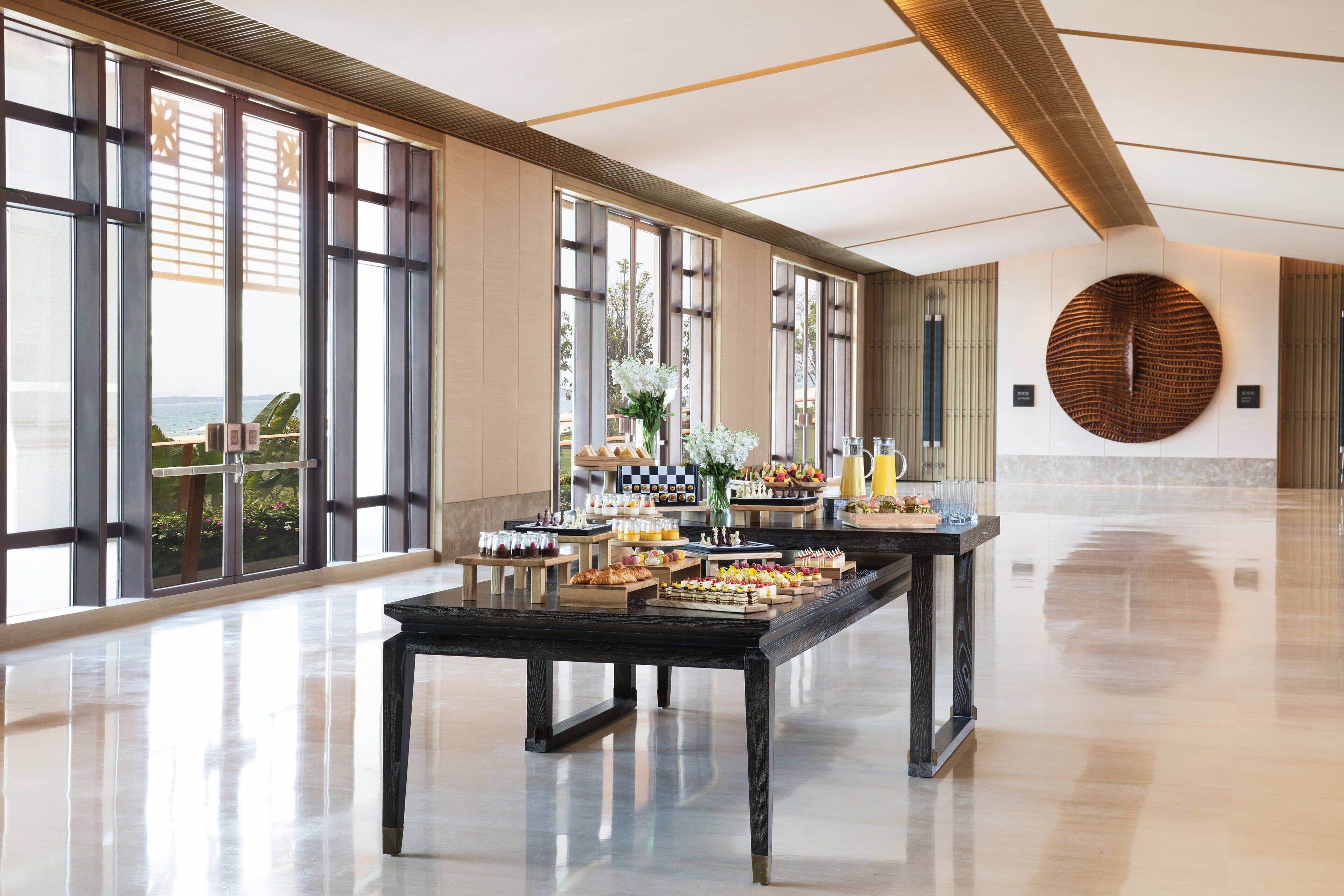 A spacious room with large windows, a polished floor, and a buffet table with various food items.