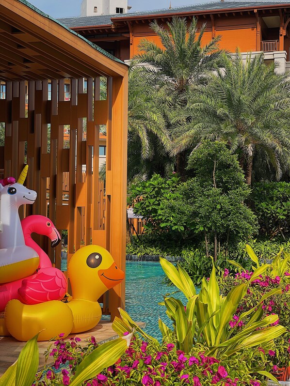 A pool area with inflatable toys, a wooden deck, and lush greenery.