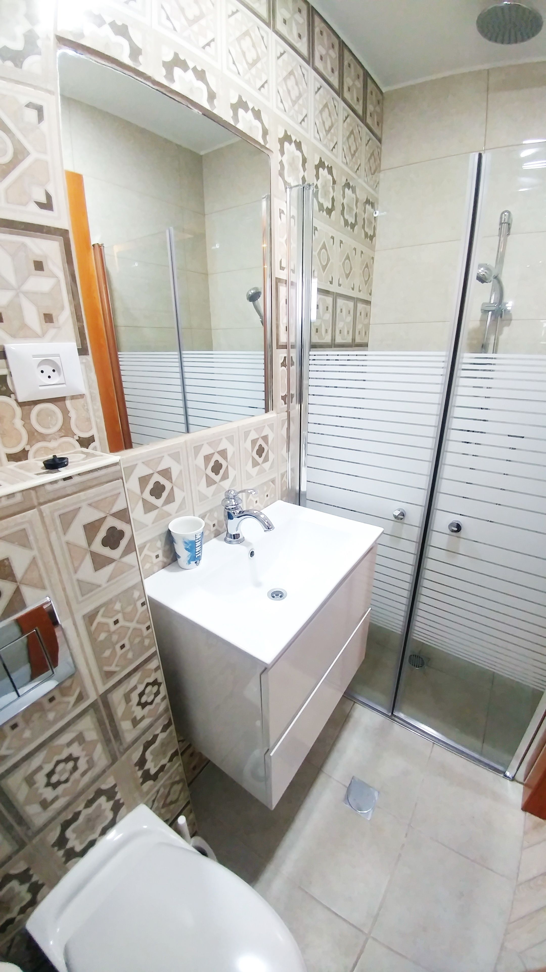 A bathroom with a white sink, a mirror, a shower enclosure, and patterned tiles.