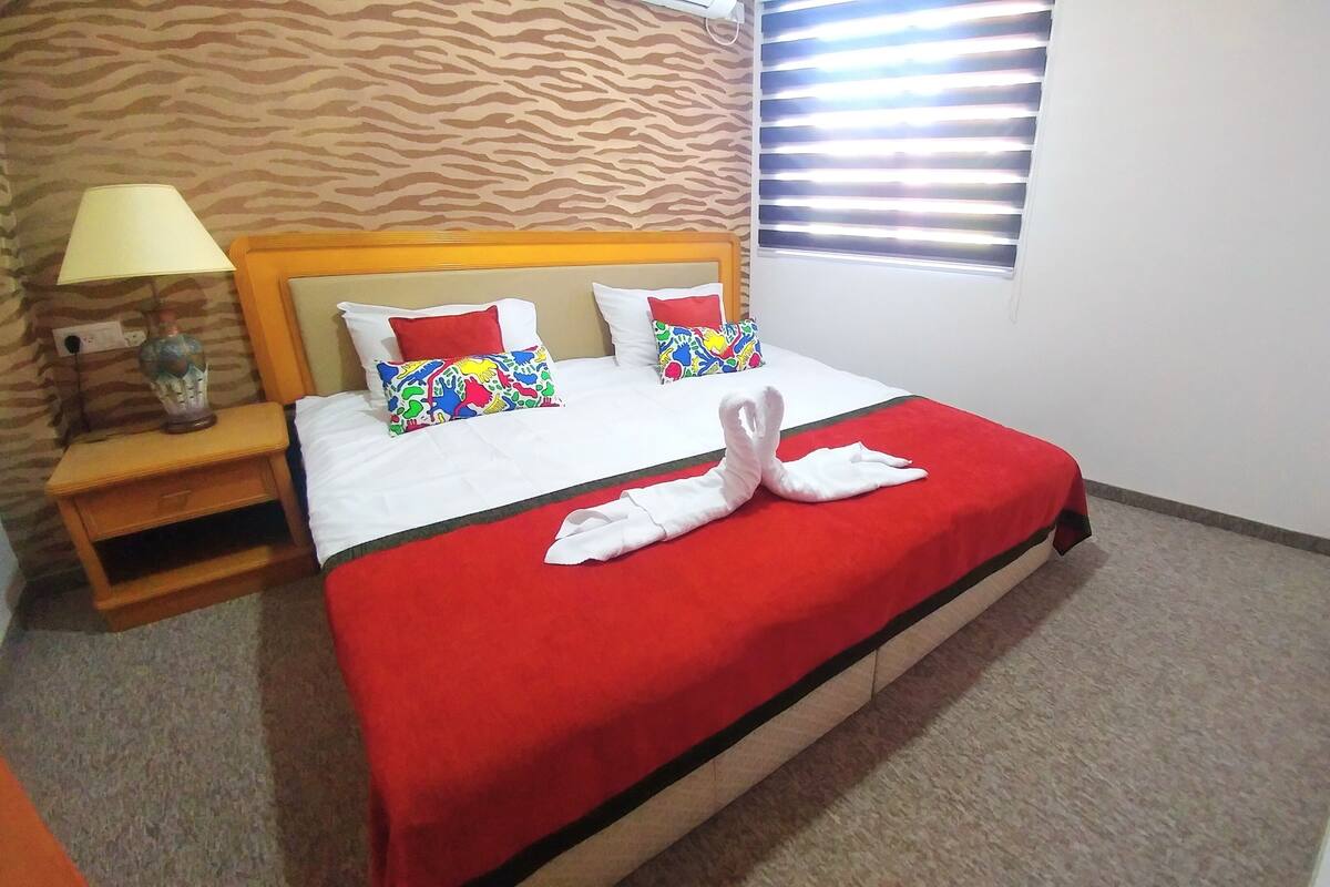 Una habitación de hotel con cama, mesita de noche, lámpara y ventana con persianas.