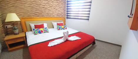 A hotel room with a bed, a nightstand, a lamp, and a window with blinds.