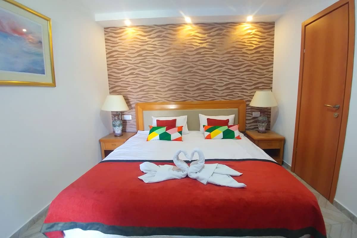 Una habitación de hotel con una cama, dos mesitas de noche, una puerta de madera y una pared con estampado de cebra.