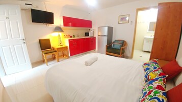 A hotel room with a bed, a desk, a chair, a TV, a red cabinet, a microwave, and a refrigerator.