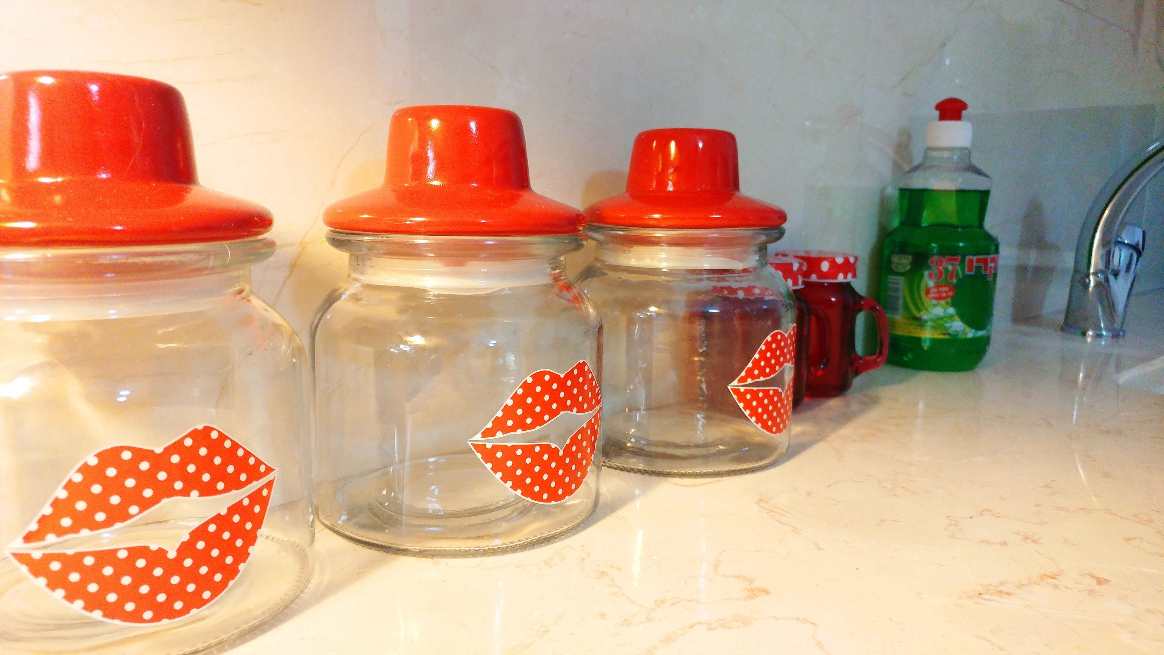 Three glass jars with red lids and red polka-dotted labels on a kitchen counter.