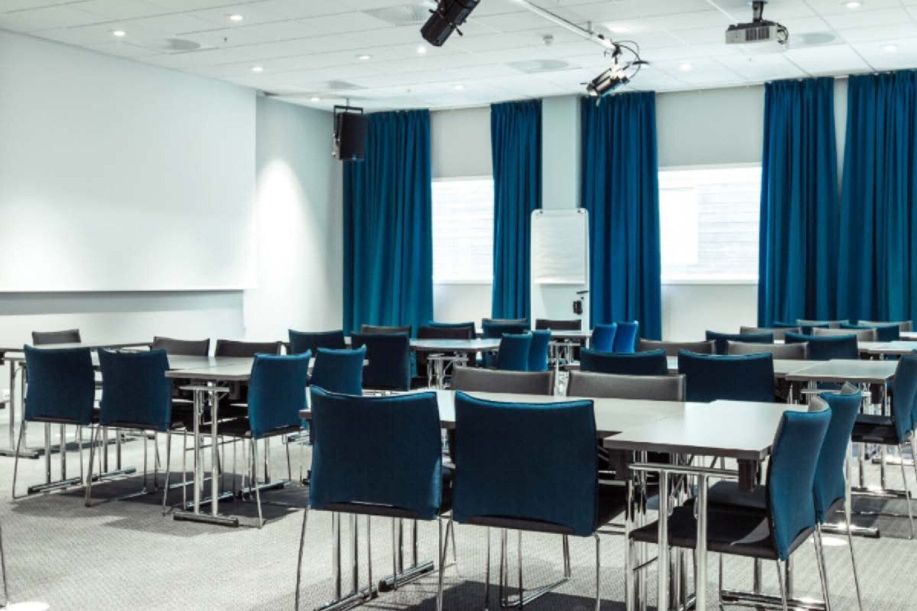 A conference room with tables and chairs, a whiteboard, and blue curtains.