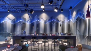 A modern bar area with a unique sound-absorbing wall design, bar stools, and ambient lighting. - X Hotel (Lillestrom)