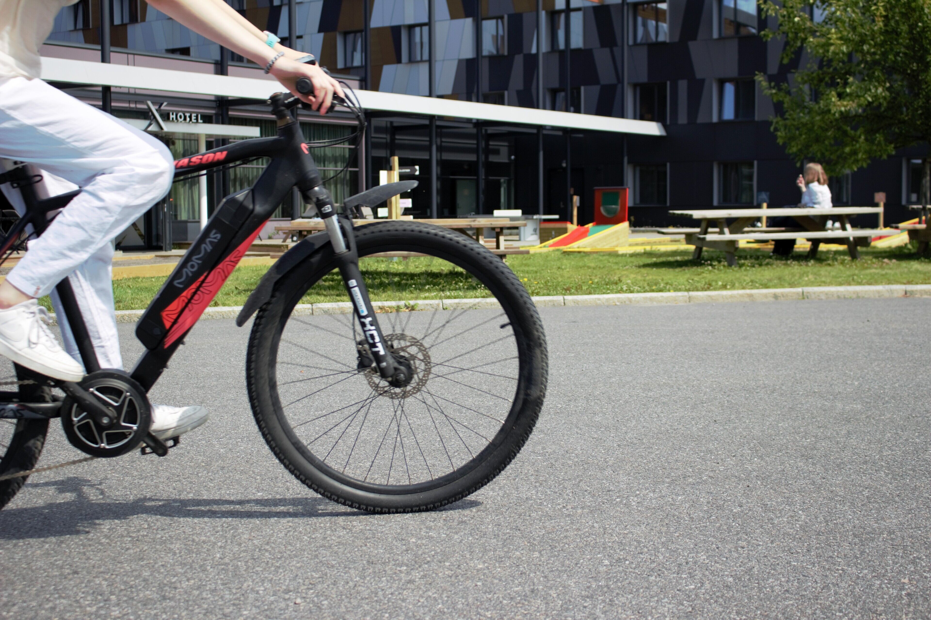 A person riding a bicycle on a paved surface with a modern building in the background.