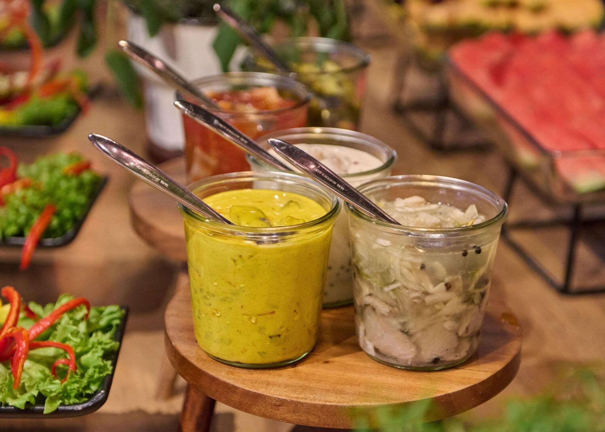 Una mesa de madera con tres frascos de vidrio que contienen diferentes alimentos, cada uno con una cuchara.