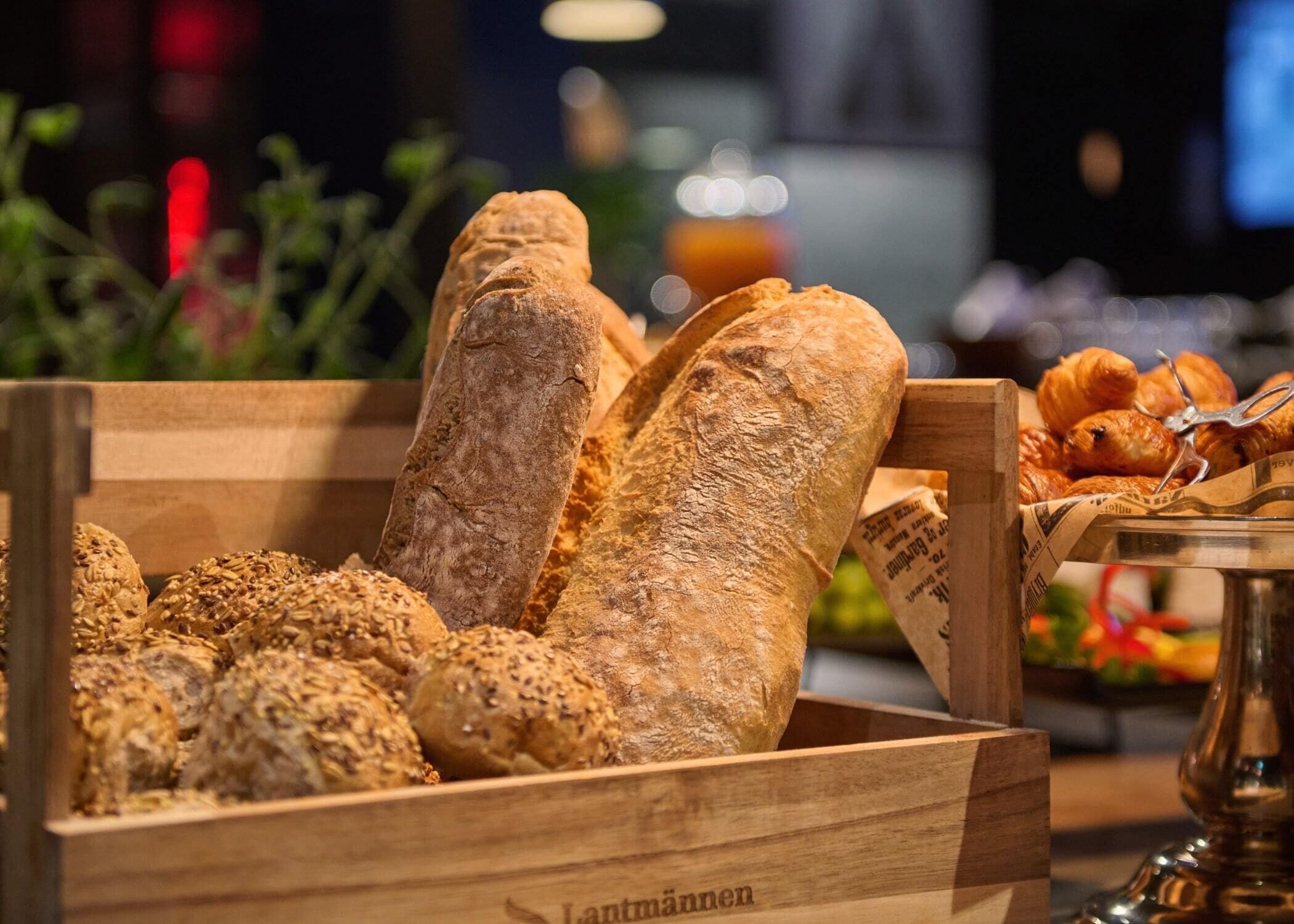 A wooden crate filled with various types of bread, including baguettes and seeded rolls.