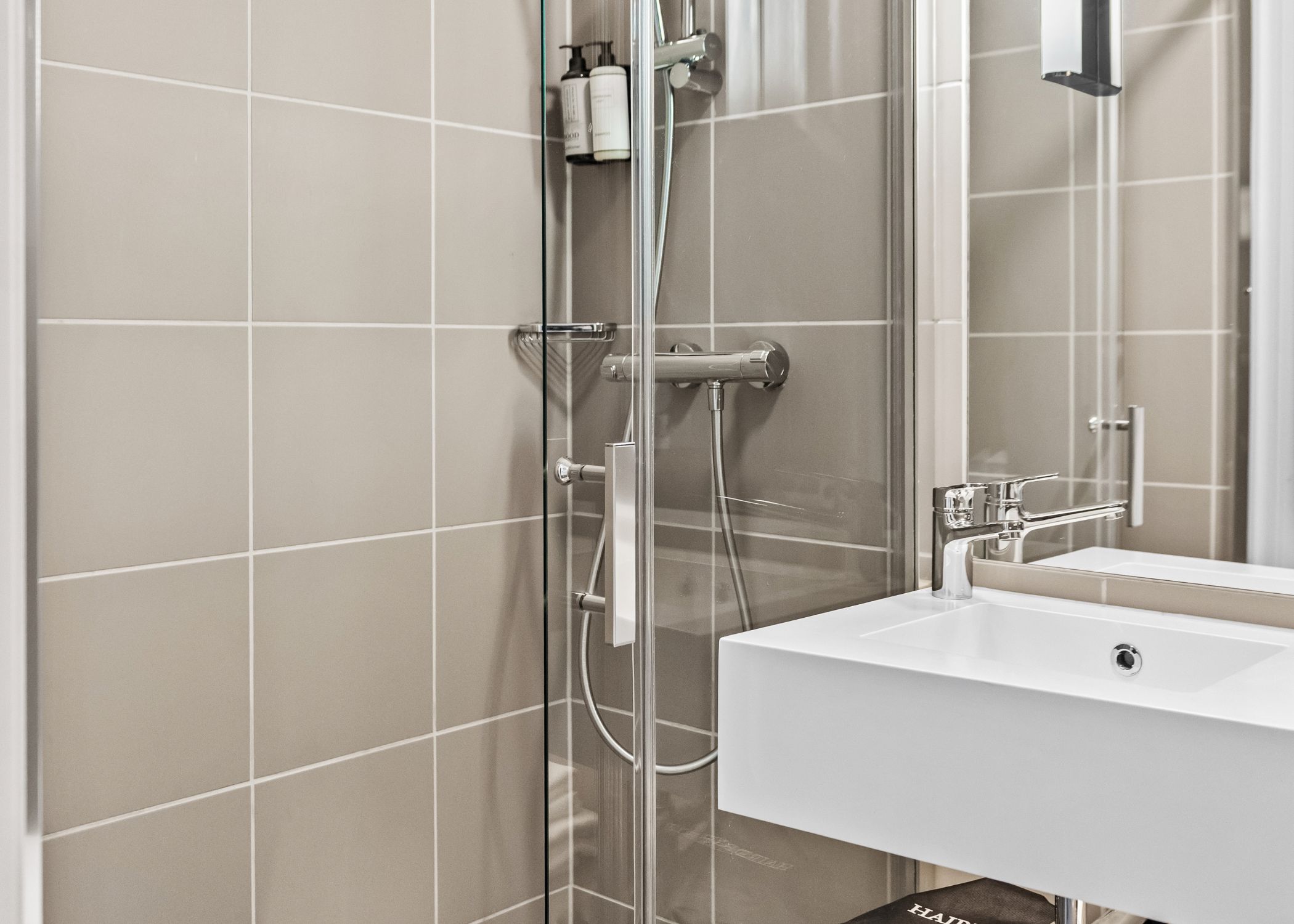A modern bathroom with a glass shower enclosure, a white sink, and a mirror.