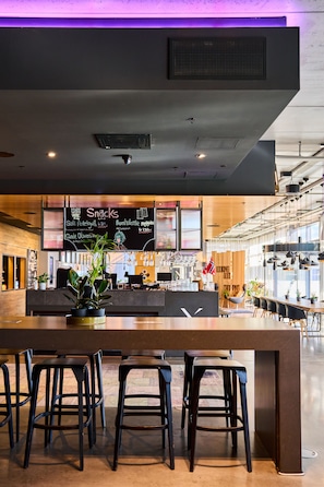 A bar area with a long counter, multiple stools, and a menu board above. - X Hotel (Lillestrom)