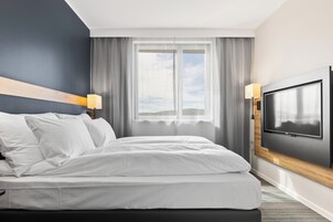 Habitación de hotel con cama, televisor montado en la pared y ventana con cortinas.