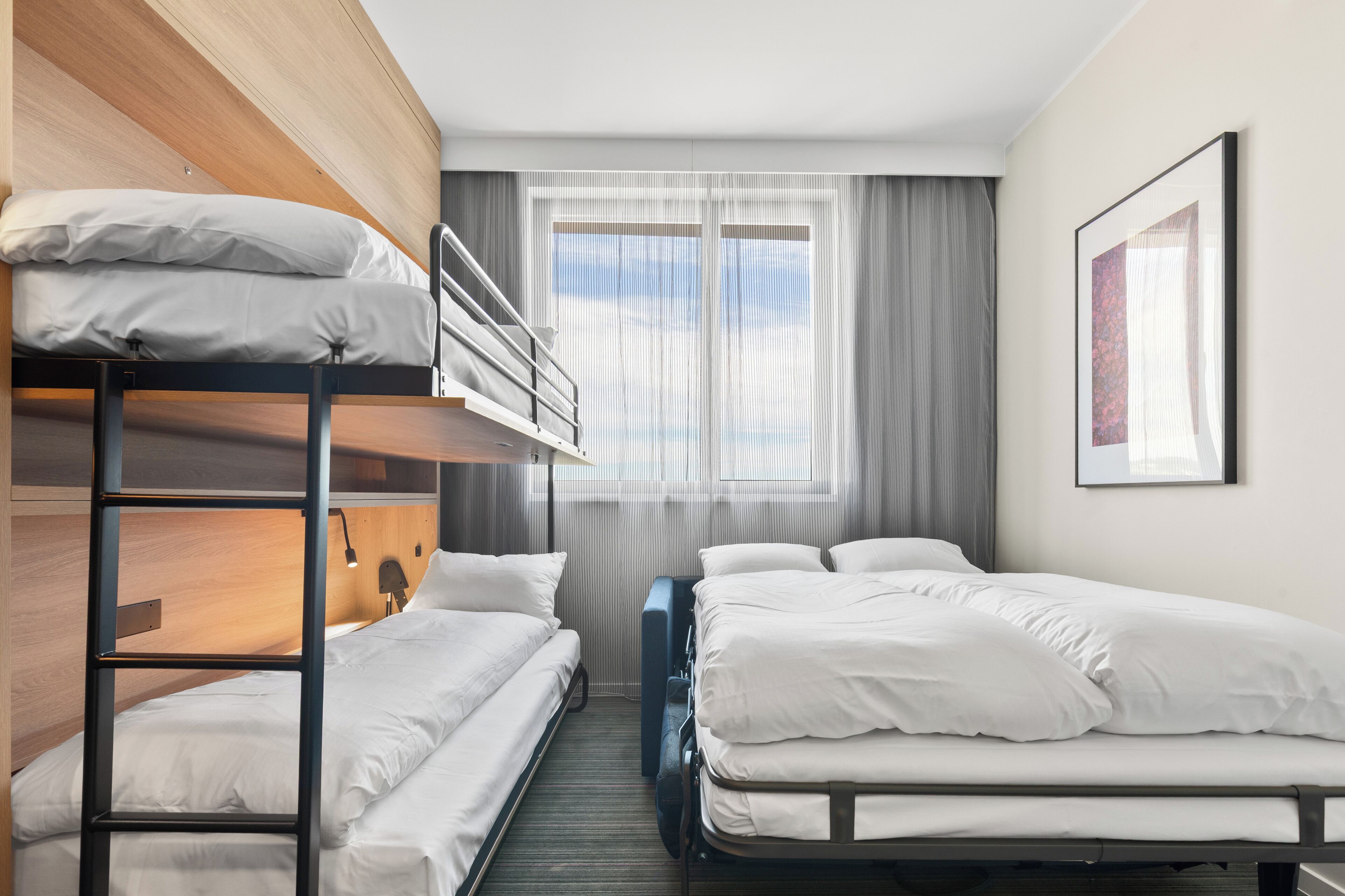 Une chambre d’hôtel avec des lits superposés, un lit simple, un bureau et une fenêtre avec des rideaux.