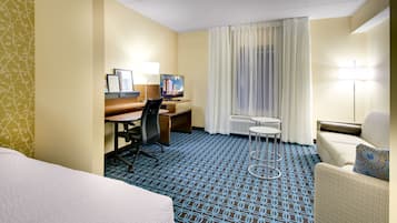 A hotel room with a bed, a desk, a chair, a small table, and a sofa.