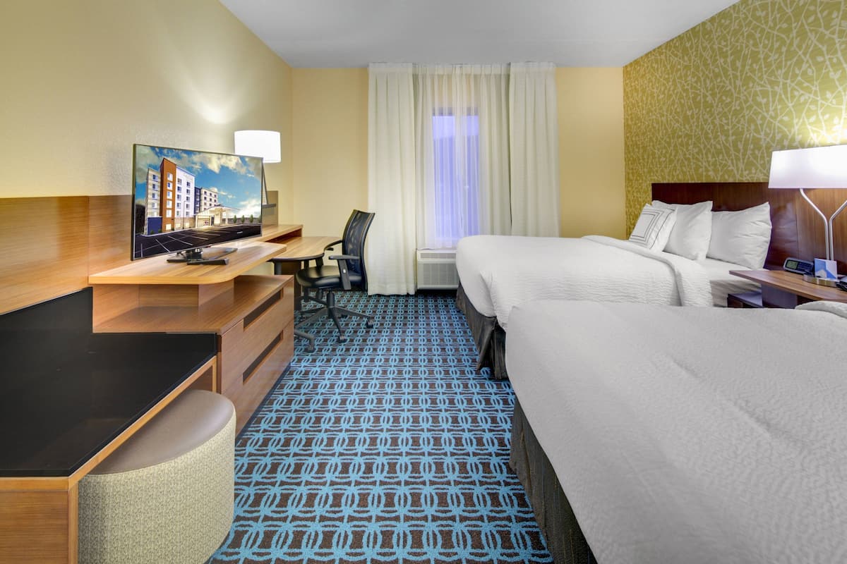A hotel room with a bed, desk, chair, and a painting on the wall.
