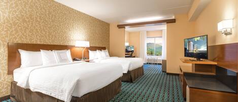 A hotel room with two beds, a TV, a desk, and a view of the outdoors.