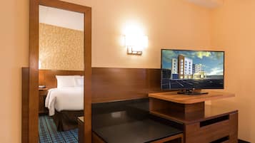 A hotel room with a bed, a TV on a wooden stand, a mirror, and a wall-mounted light.