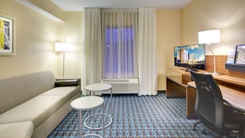 A hotel room with a sofa, a small round table, a TV, a desk, and a chair.