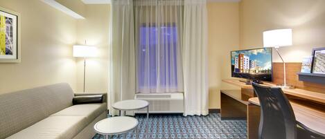 A hotel room with a sofa, a small round table, a TV, a desk, and a chair.