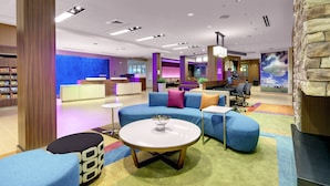 A modern hotel lobby with a reception desk, seating area with sofas and ottomans, a small round table with a bowl, and a stone accent wall. - Fairfield Inn & Suites by Marriott Asheville Tunnel Road (Asheville)