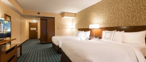 Habitación de hotel con dos camas, televisor, escritorio y alfombra estampada.