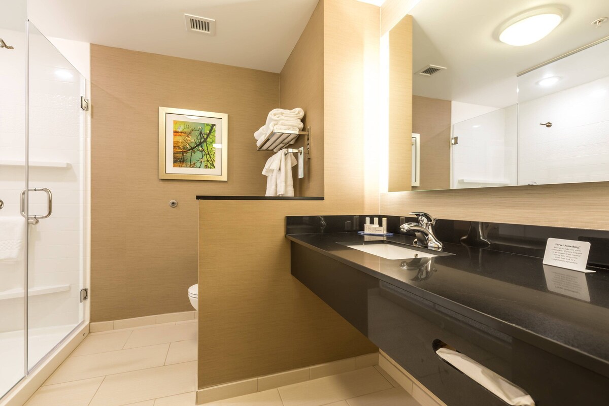 A modern bathroom with a black countertop, a sink, and a mirror. There is a towel rack with towels and a framed picture on the wall.