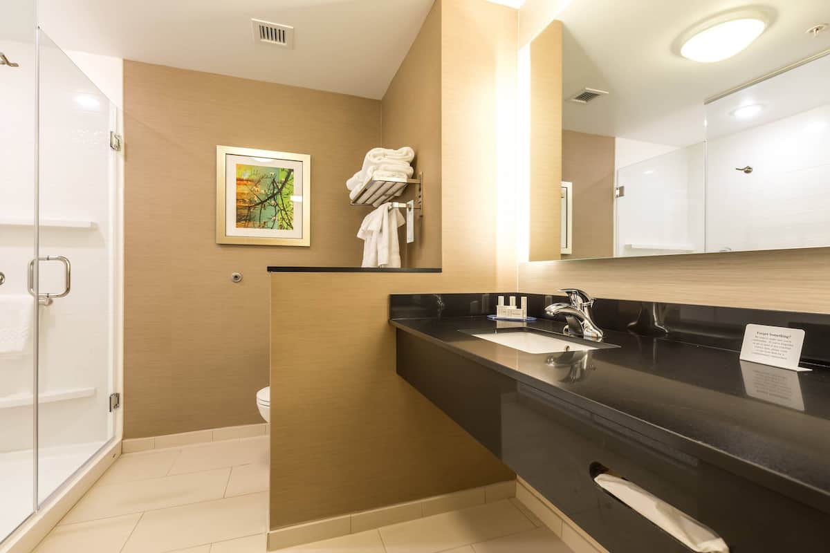 A modern bathroom with a black countertop, a sink, and a mirror. There is a towel rack with towels and a framed picture on the wall.