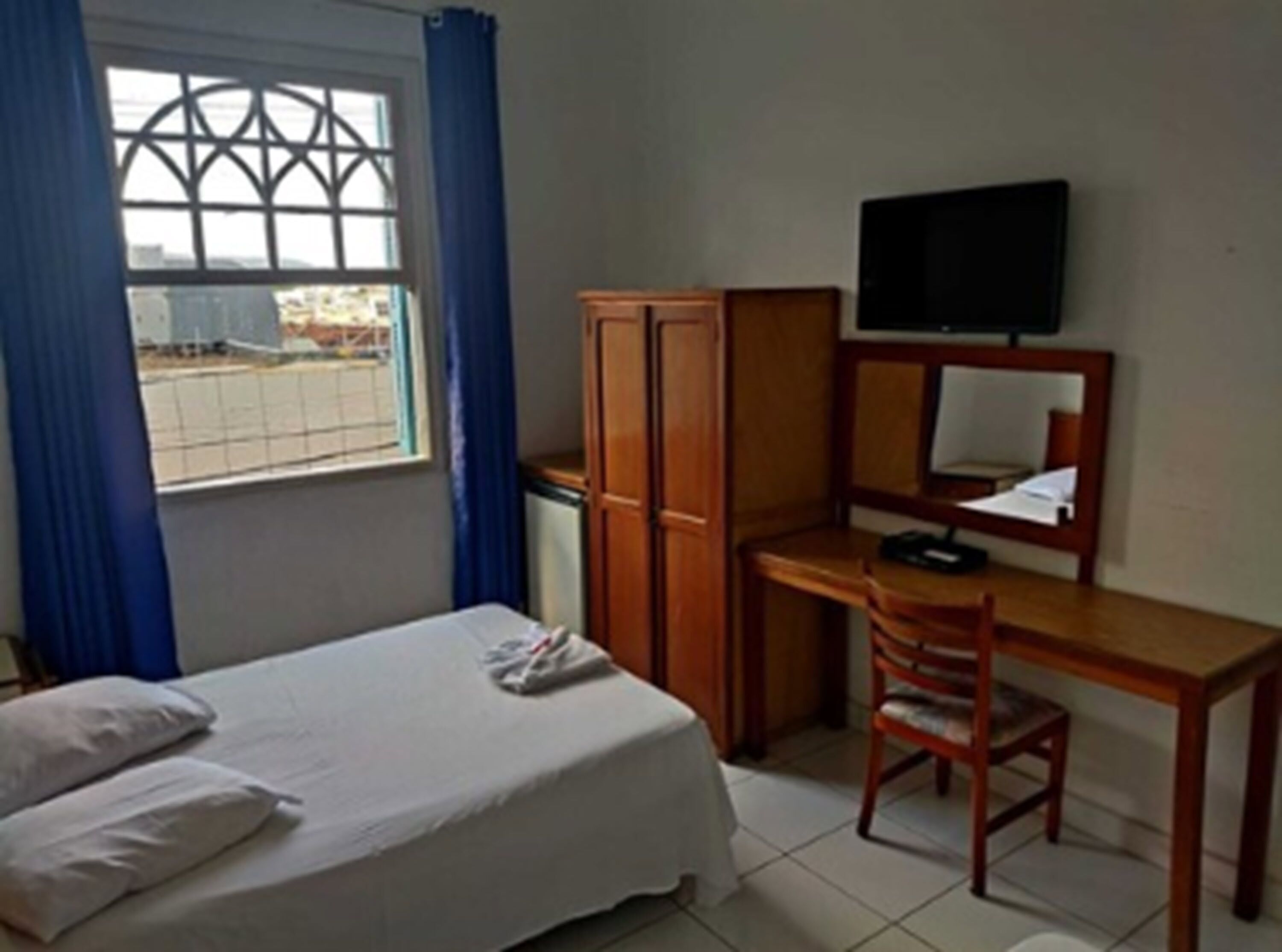 A hotel room with a bed, a desk with a chair, a television, and a wardrobe.