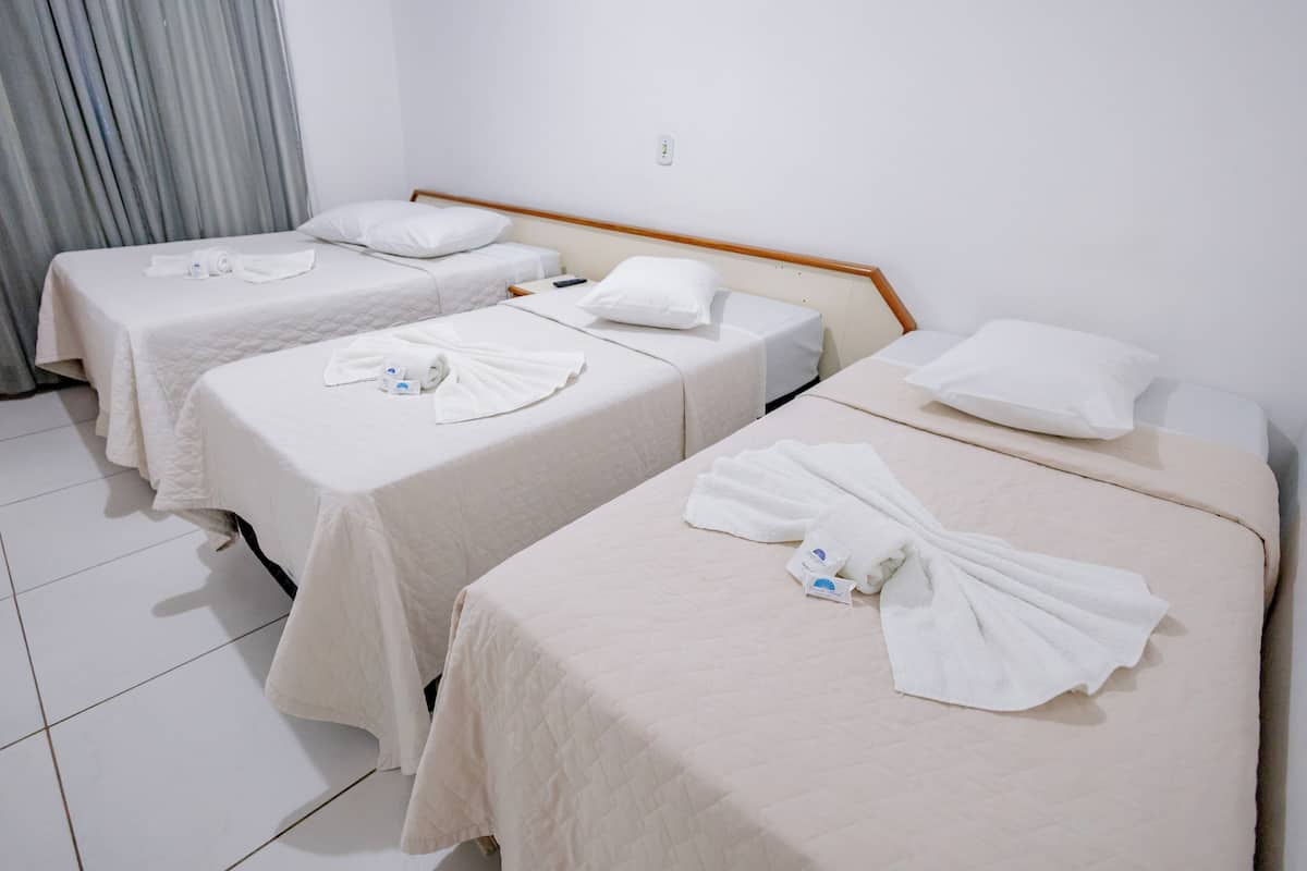Habitación de hotel con tres camas, cada una con colcha y almohadas blancas, y cabeceros de madera.