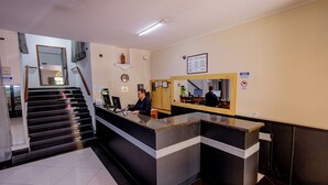 Un espace d’accueil d’hôtel comprenant un comptoir, un réceptionniste, un escalier et un miroir fixé au mur.