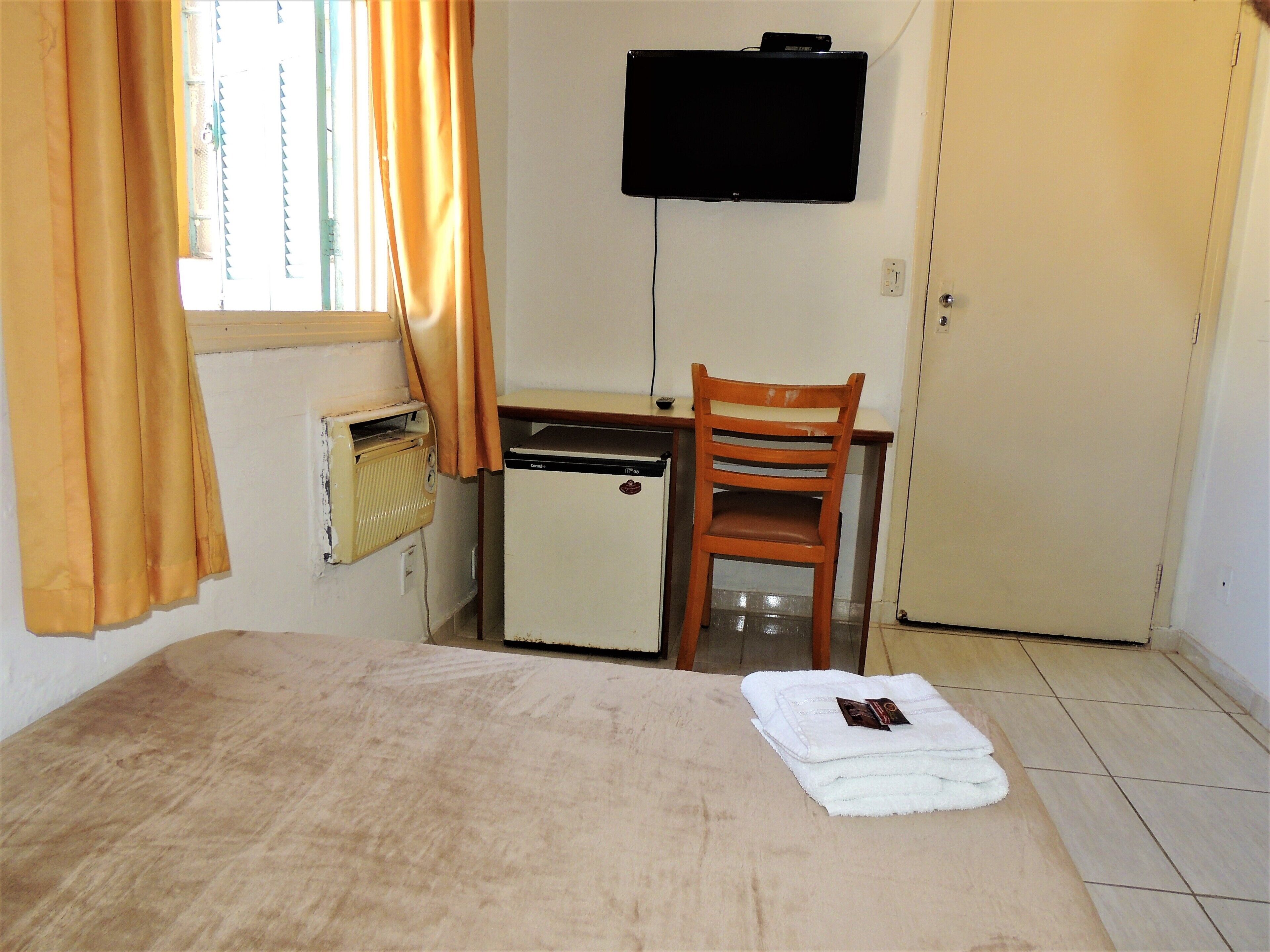 Una habitación pequeña con cama, escritorio, silla, televisión y radiador.