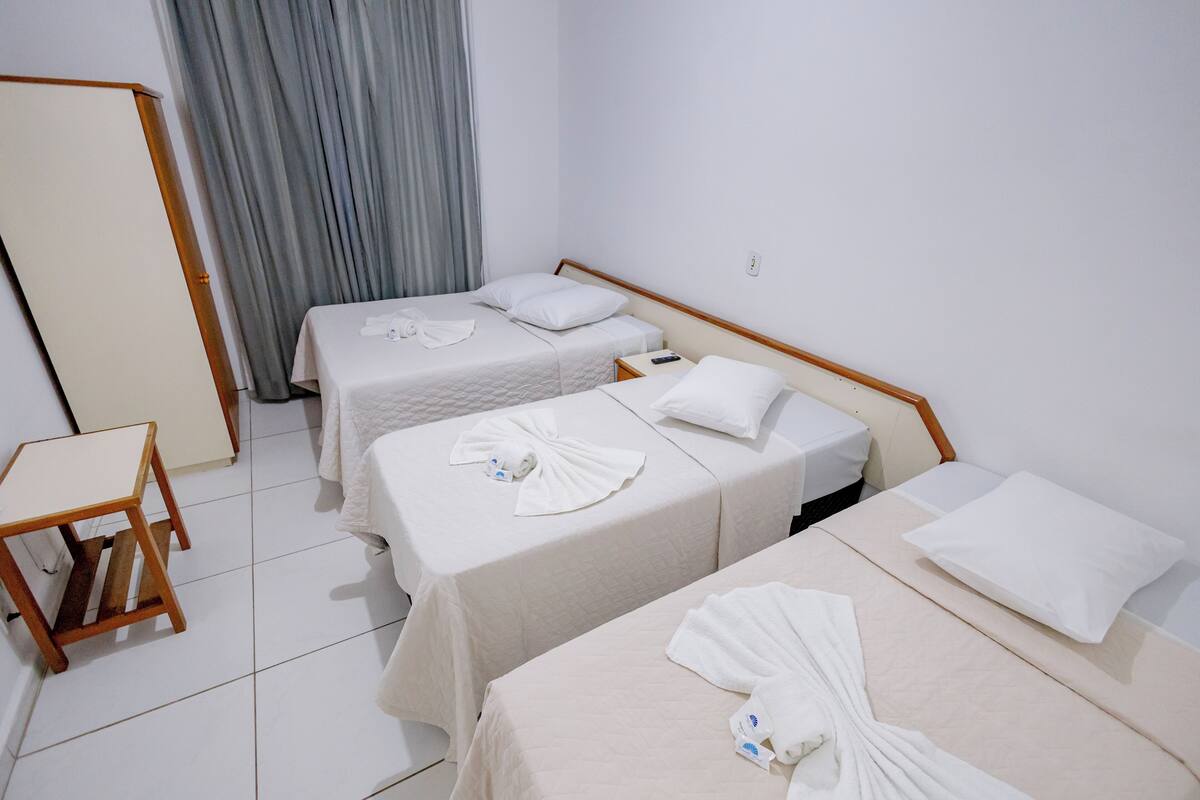 Una habitación de hotel con dos camas individuales, una mesita de noche de madera, una pequeña mesa y una cortina gris.