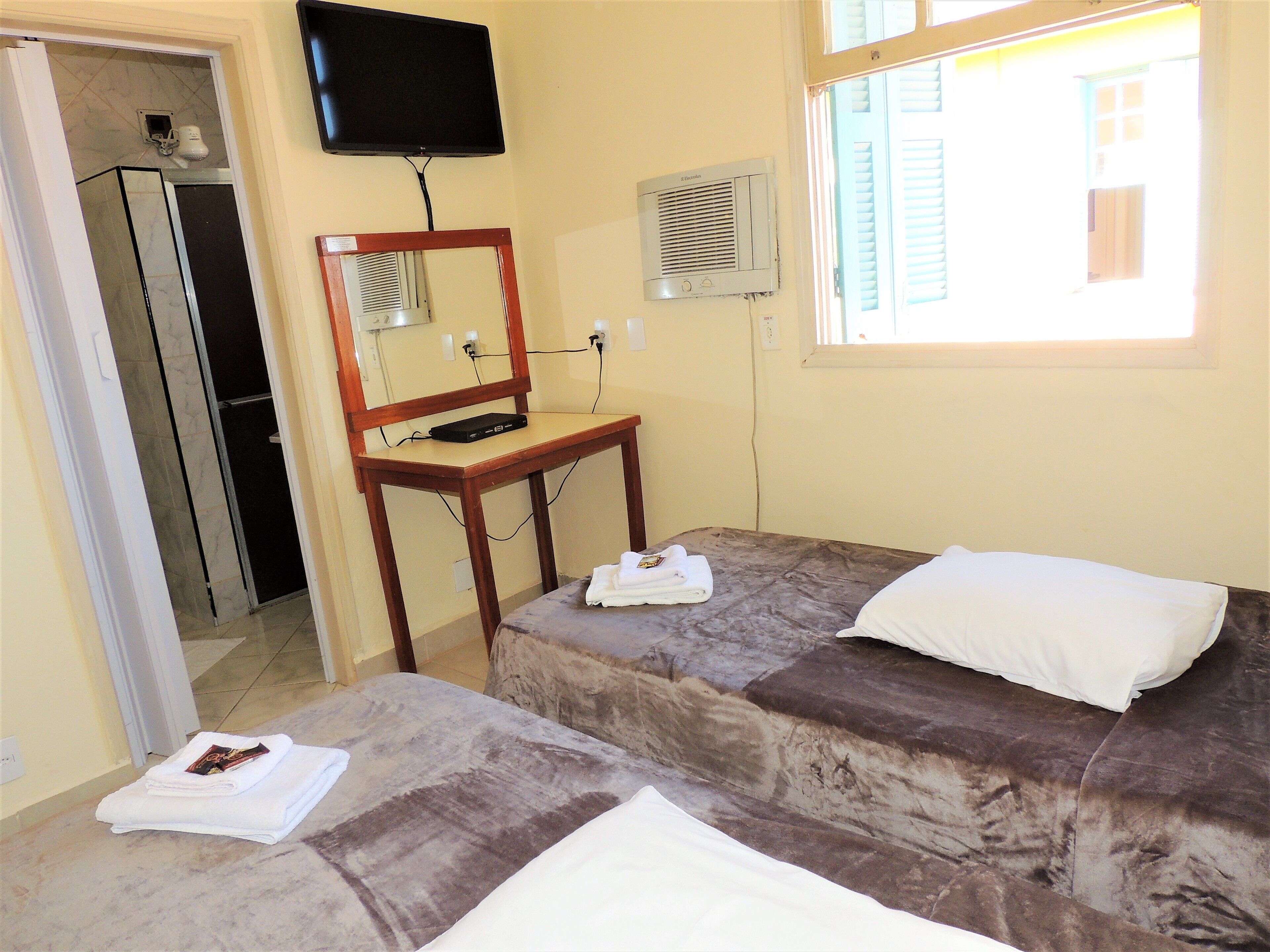A room with two beds, a television, a mirror, and a window.