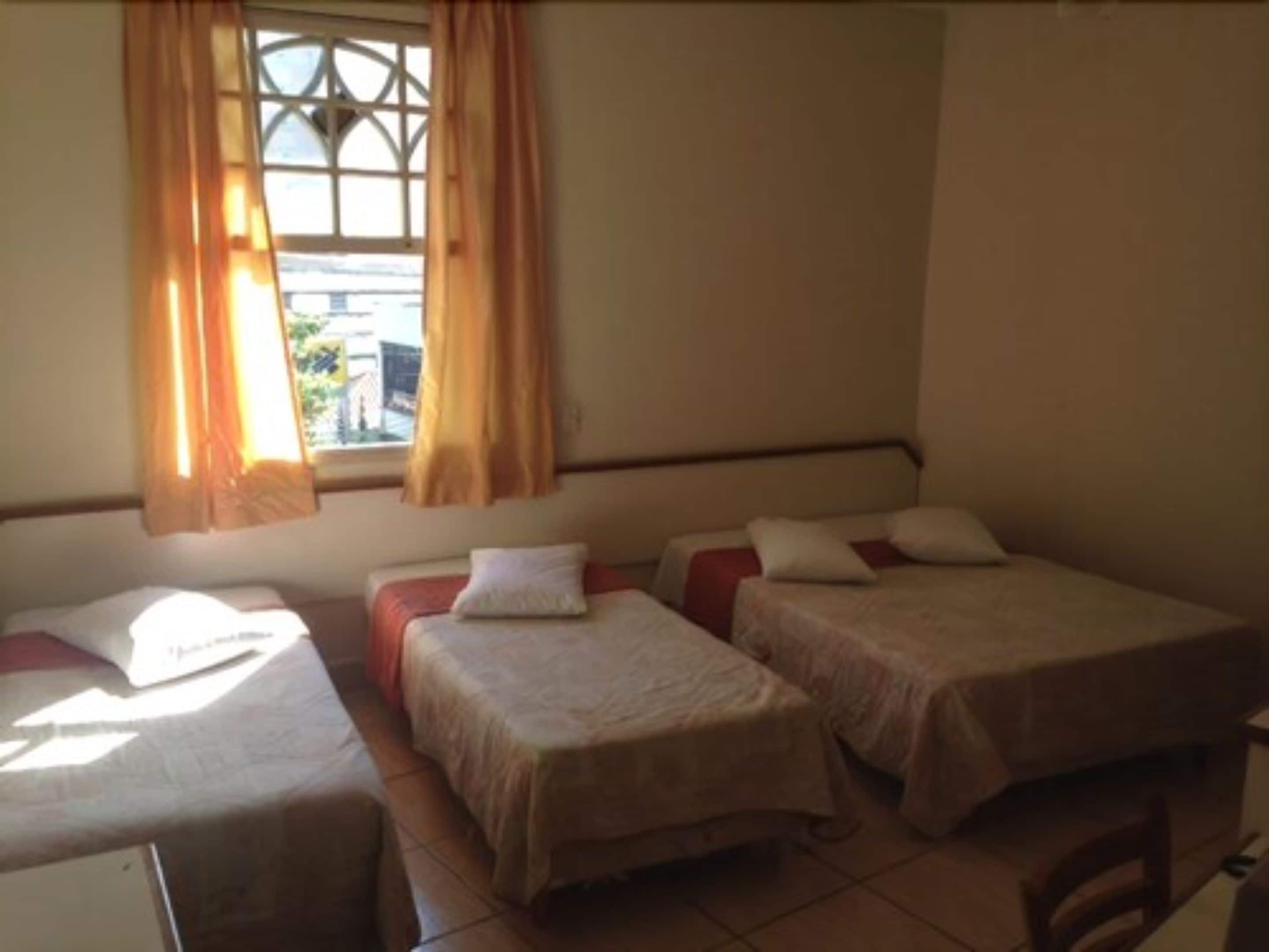A small, simple room with two single beds, a window with curtains, and a tiled floor.
