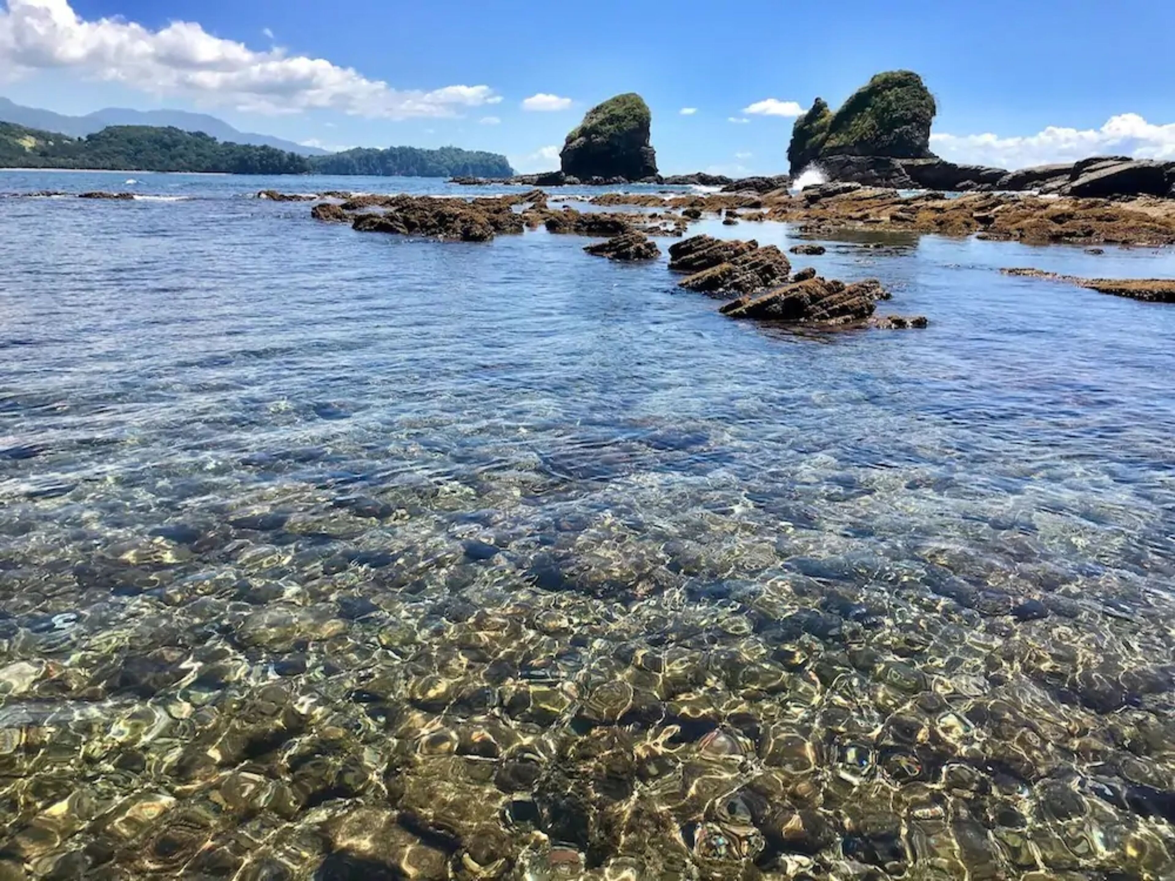 Una vista despejada de una costa rocosa con agua tranquila y montañas a lo lejos.