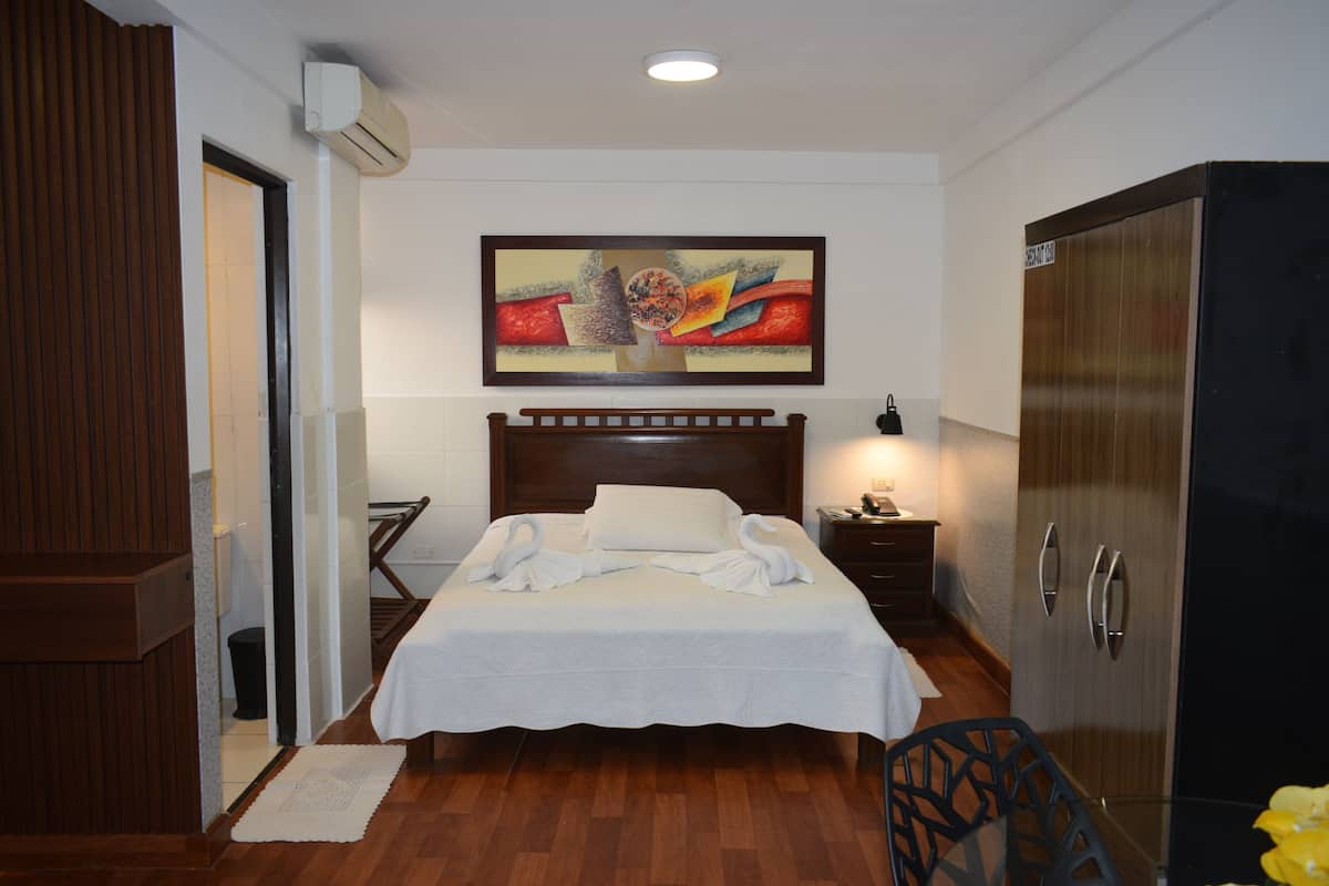 Una habitación de hotel con cama, mesita de noche, armario y un cuadro en la pared.