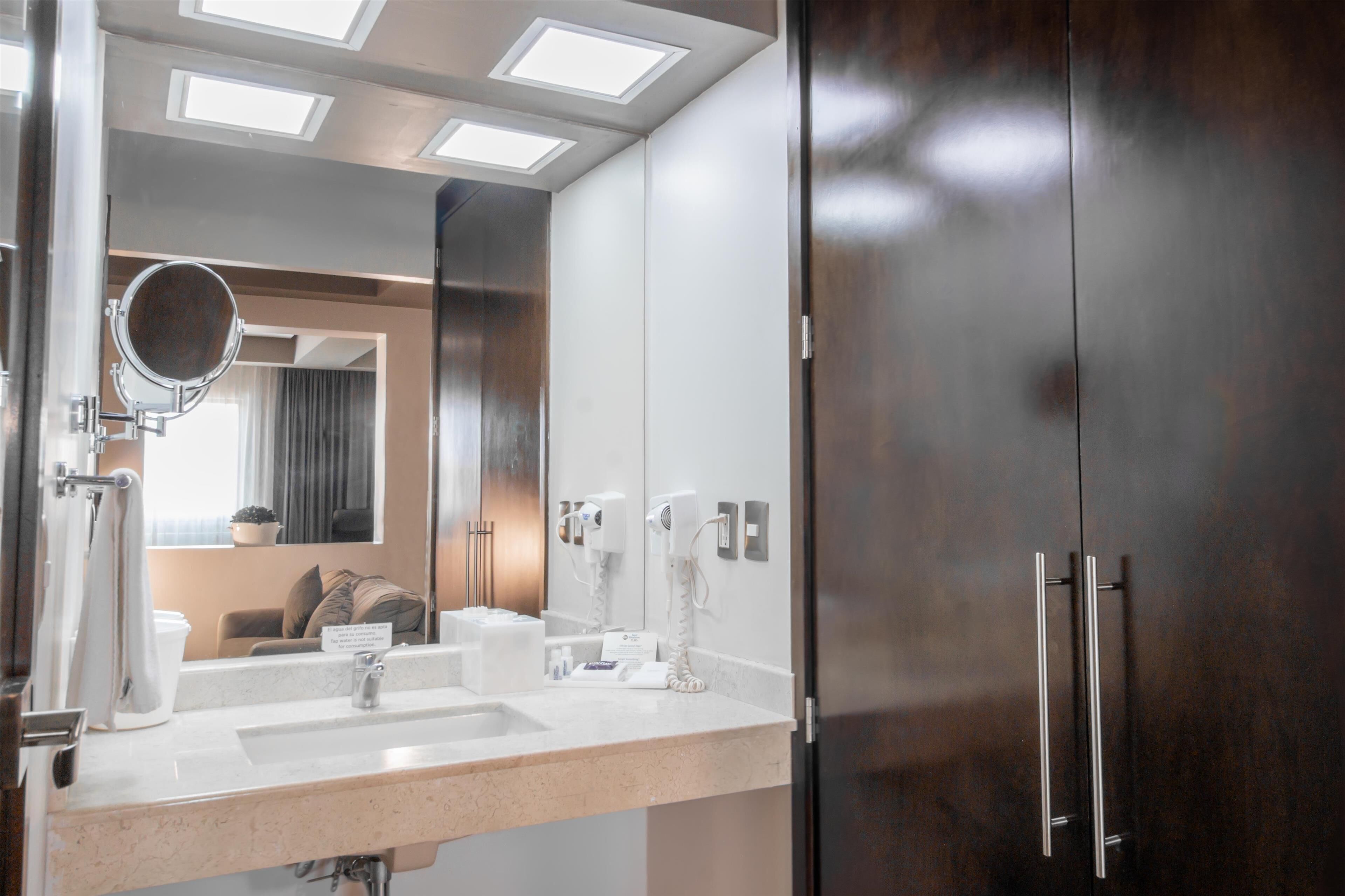 Une salle de bain moderne avec un grand miroir, un lavabo et un sèche-cheveux.