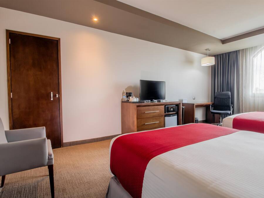 Una habitación de hotel con dos camas, un escritorio con televisor, una silla y un armario.