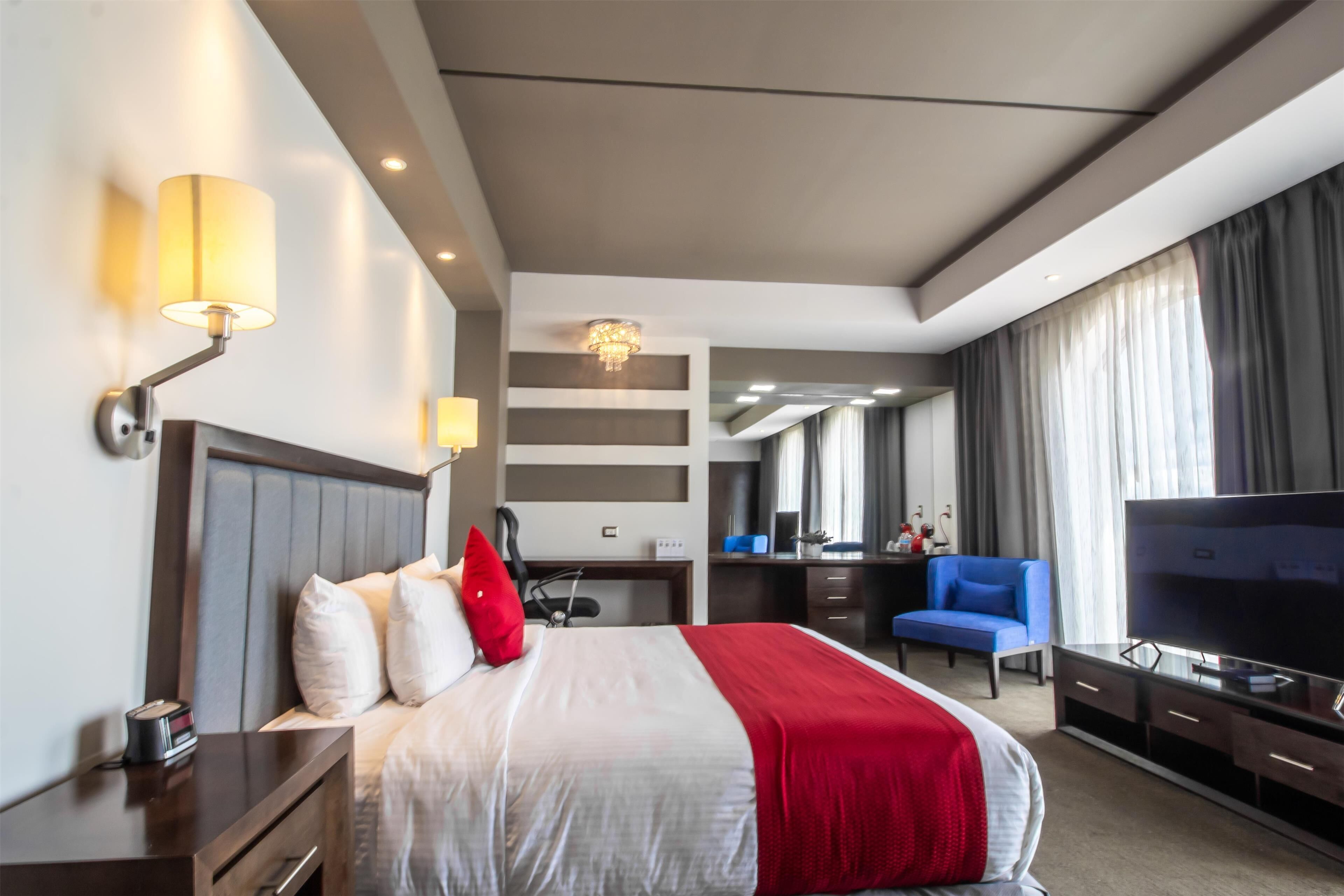A hotel room with a bed, a desk, a chair, a TV, and a large window with curtains.