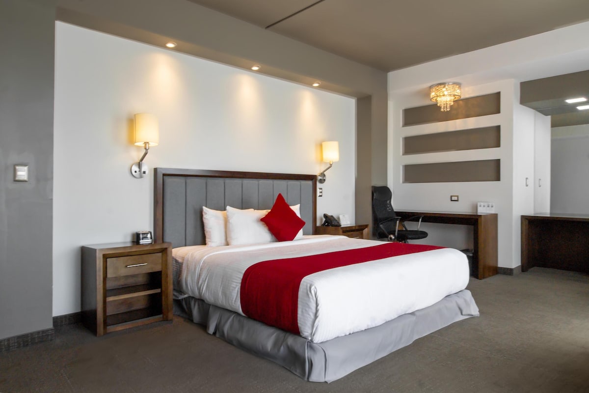 A hotel room with a bed, bedside tables, a desk, and a chair.