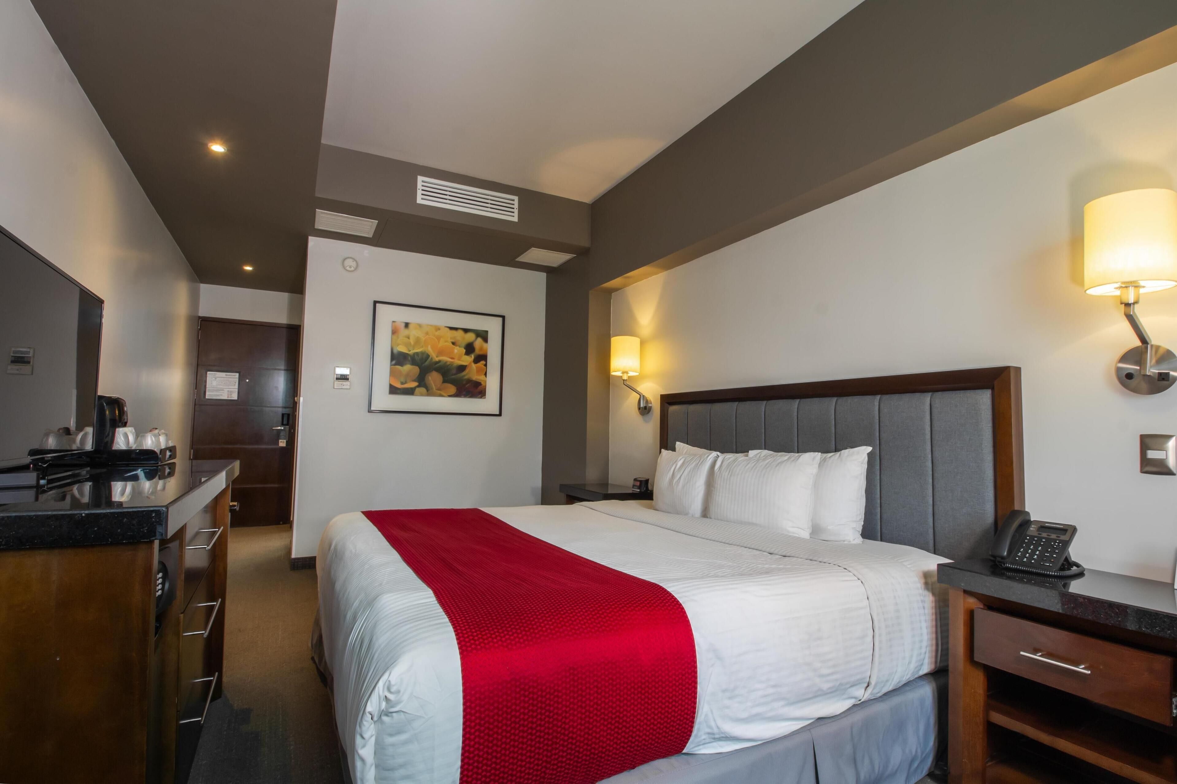Habitación de hotel con cama, mesita de noche, lámpara y un cuadro en la pared.