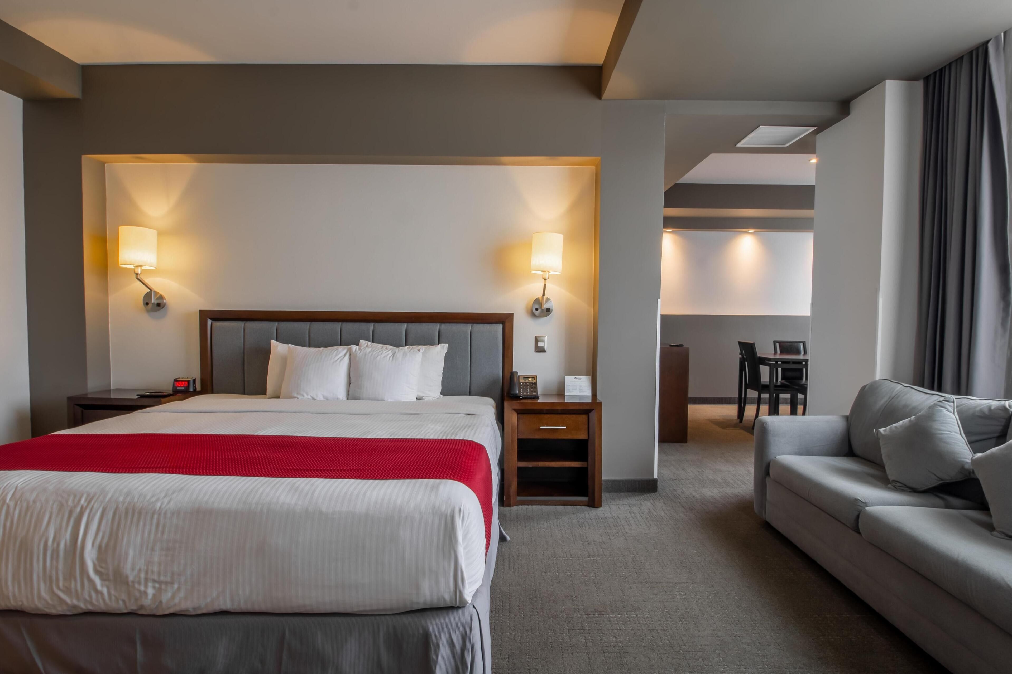Una habitación de hotel con una cama grande, un sofá, dos mesitas de noche, un escritorio y una silla.