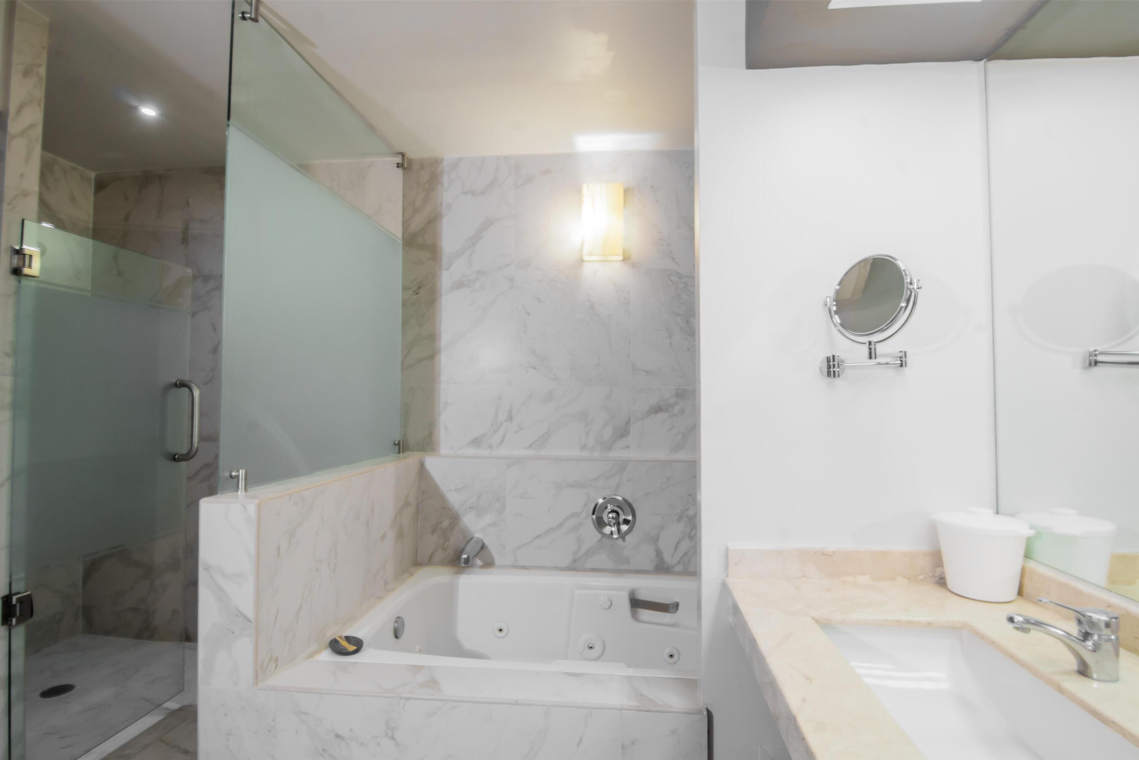 A modern bathroom with a glass-enclosed shower, a marble-tiled wall, a freestanding bathtub, and a vanity with a sink and mirror.