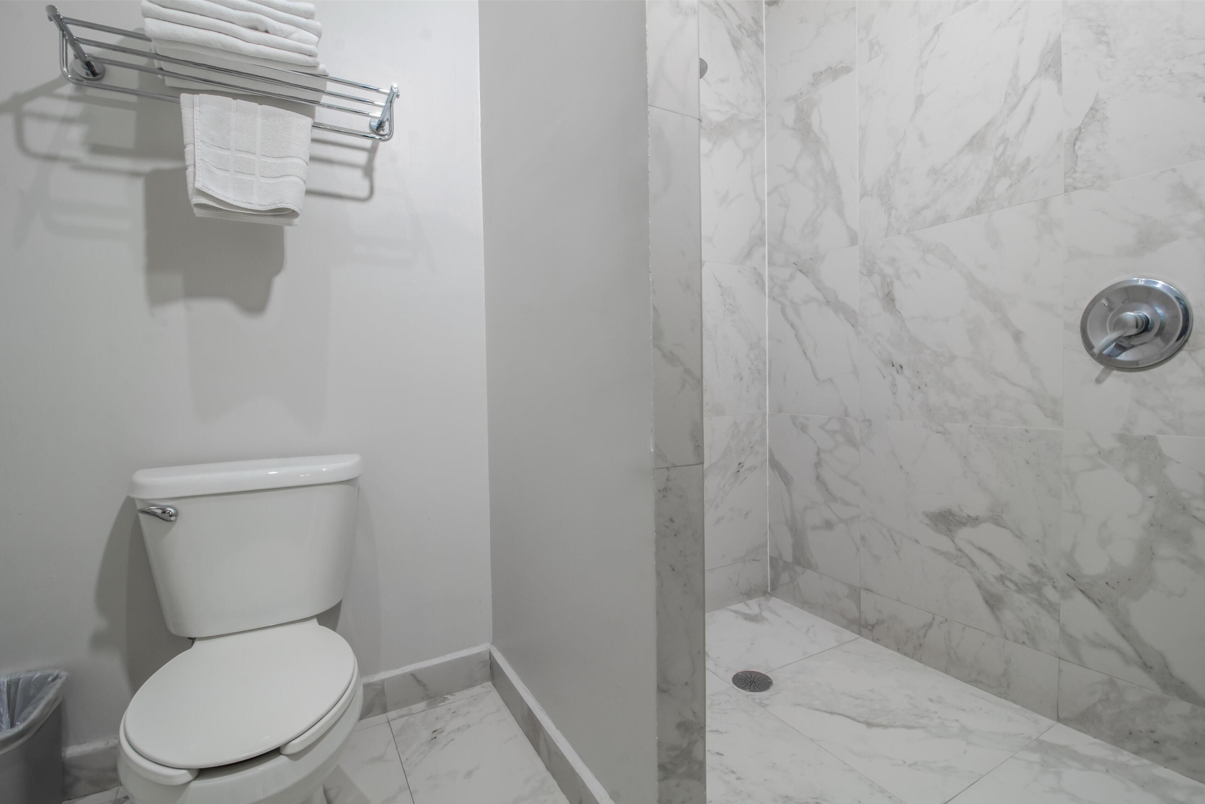 Un baño con inodoro, toallero con toallas dobladas y zona de ducha con paredes y suelo de mármol.