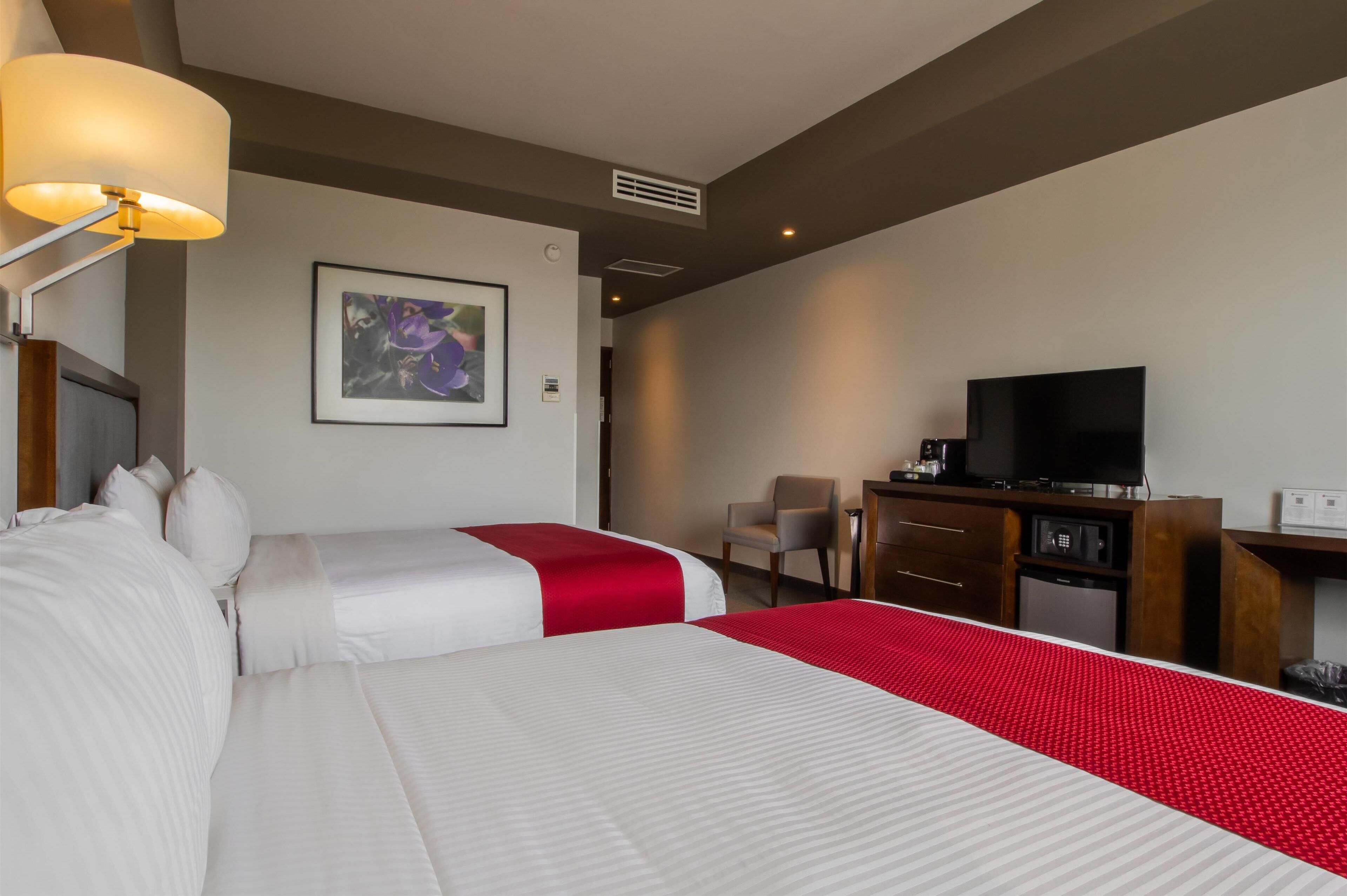 Une chambre d’hôtel avec deux lits, un bureau avec une télévision et une chaise.