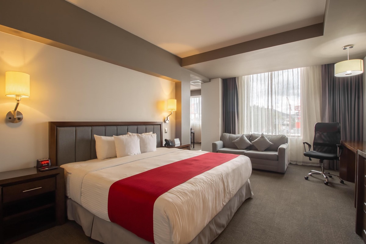A hotel room with a large bed, a sofa, a desk, and a chair.