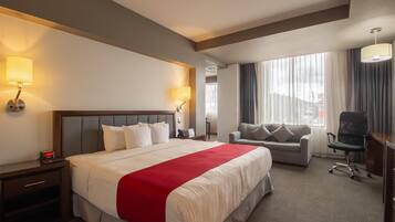 A hotel room with a large bed, a sofa, a desk, and a chair.